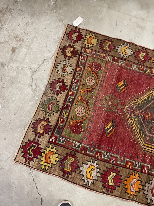 Overhead view of the red medallion rug showing olive-green floral end panels and worn pile.
