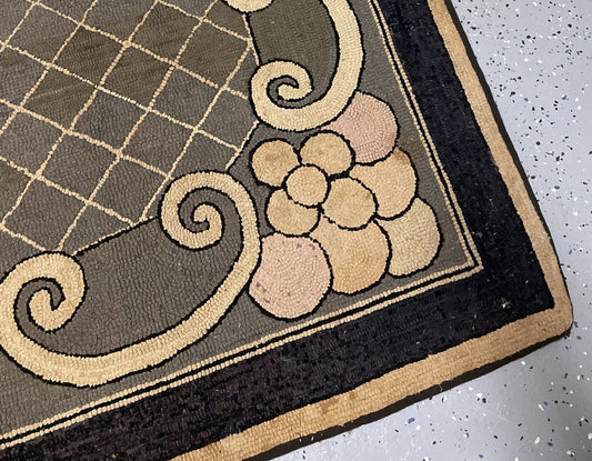 Angled rug view showing pale flowers and curling cream scrolls beside the broad charcoal border.