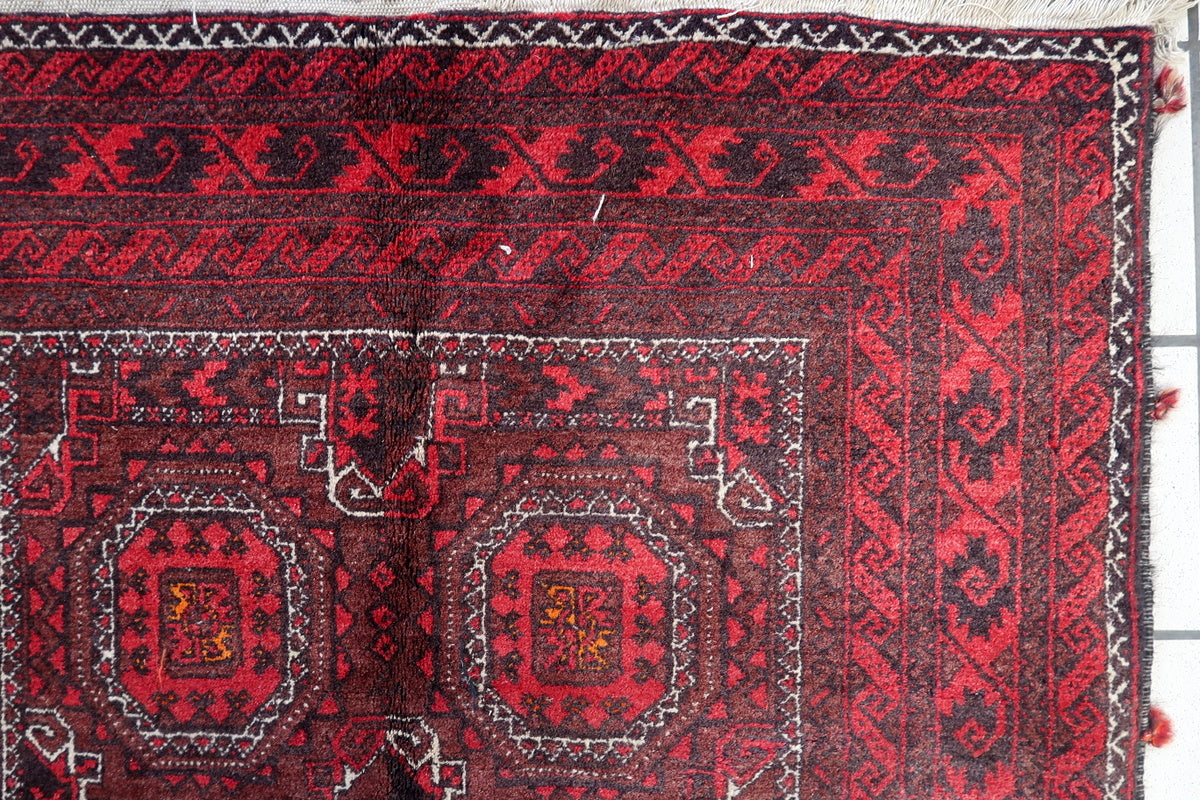 Full view of the vintage Afghan Baluch rug with vibrant red, brown, and navy colors