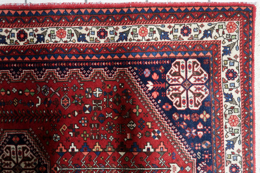 Vintage tribal rug from southern Persia with deep red field and navy borders on floor