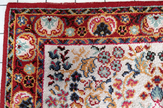 Close-up of the central medallion on a 1950s French Savonnerie rug, showing a deep crimson/ruby red center rosette with gold point, surrounded by concentric rings of dark navy scrolling acanthus forms with teal detail, and an outer ring of crimson scrolling forms with black outlines and gold accents.