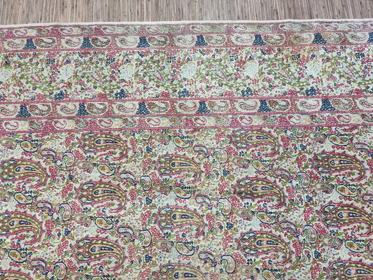 Close-up of a hand-knotted 1930s Persian Kerman carpet showing traditional floral motifs and detailed medallion design in a neutral beige palette on premium wool.