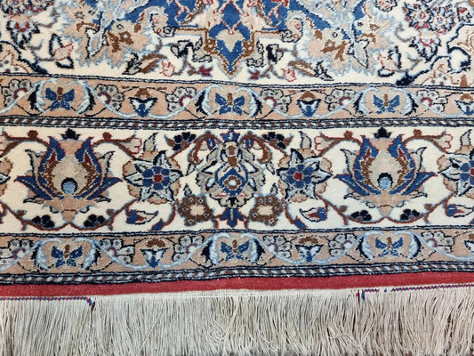 Close-up of a 1920s Persian Nain carpet showing the classic central medallion and corner spandrels with delicate floral patterns in navy, blue, and beige, with fine wool texture from high-knot-density weaving.