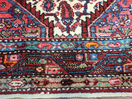 Close-up of a 1950s Persian Hamadan carpet showing the classic central medallion and corner spandrels with detailed floral patterns in navy, ivory, and gold against a deep red background.
