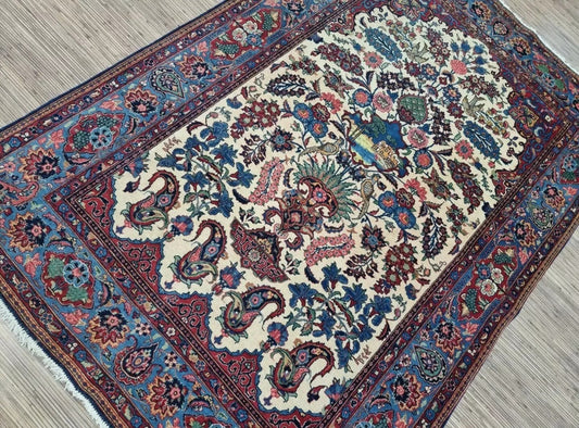 Close-up of a 1920s Persian Kashan carpet showing the detailed central medallion with floral arabesques and vine scrolls in soft beige, navy, and cream tones, with high knot density for intricate detailing.