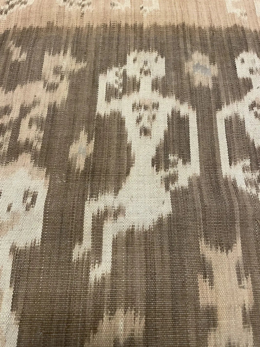 Close-up of a museum-quality hinggi kombu (men's ceremonial cloth) from Sumba Island, showing stylized human ancestor figures with outstretched arms rendered in the feathered, bleeding lines of warp ikat resist-dyeing.