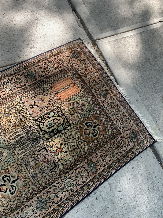 Vintage Persian silk area rug in muted gold, navy, and cream tones.