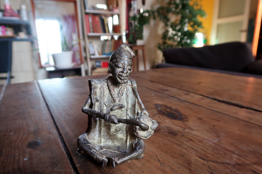 Handcrafted bronze and brass alloy statue depicting a traditional African musician playing a ceremonial hand drum.