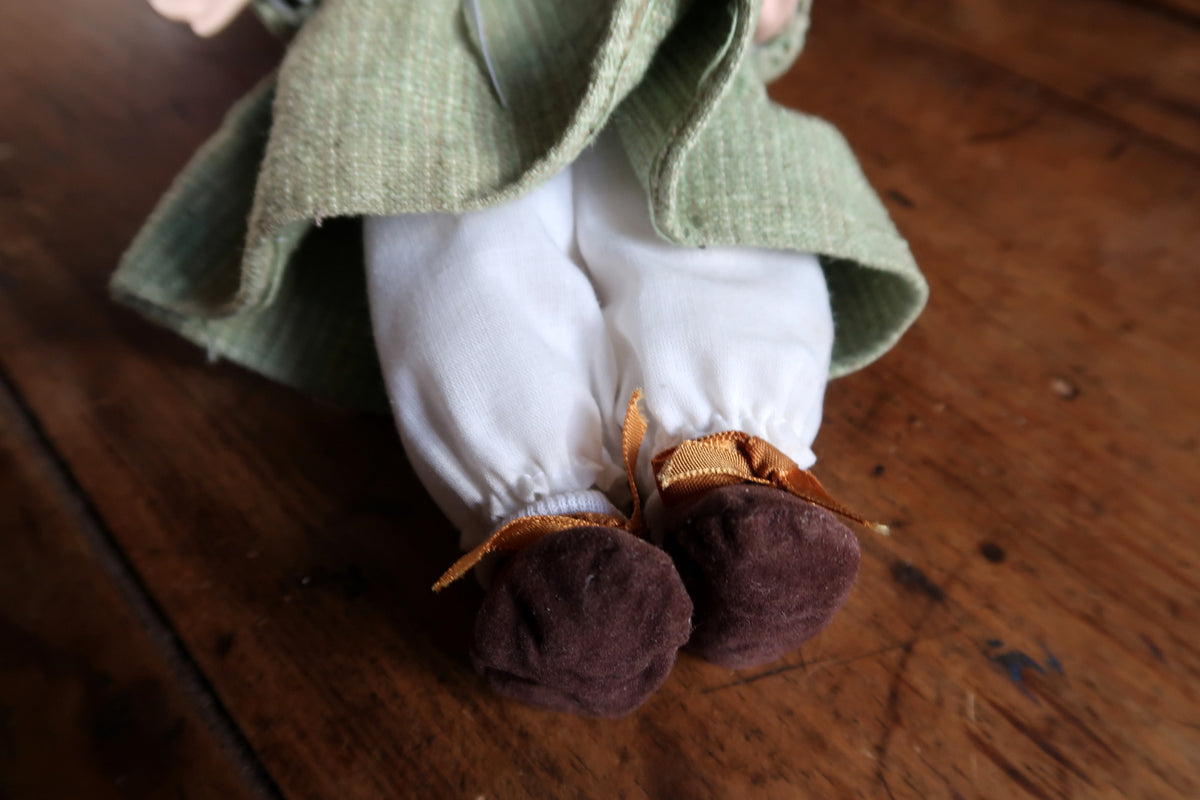 Full rear view of the doll with flower-trimmed hat, green skirt and white bloomers.