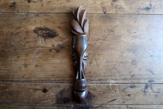 Three-quarter view highlighting the fluid polish, slender profile, and radiating leaf-petal crown of a hand-carved African hardwood wall sculpture.