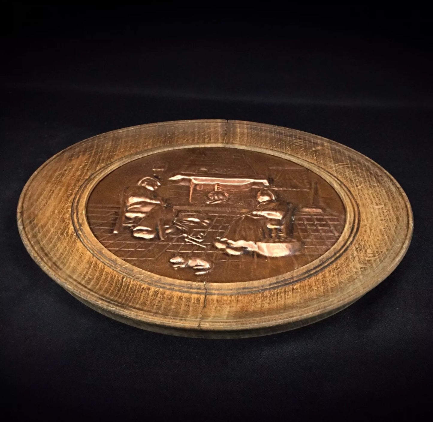 Warm copper tones and natural wood grain on a vintage French wall plate with bas-relief botanical or figurative motifs