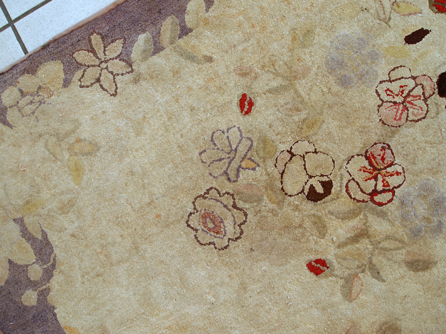 Handmade antique American Primitive Hooked rug in beige shade with abstract/floral design. The border is purple. It is in good condition.