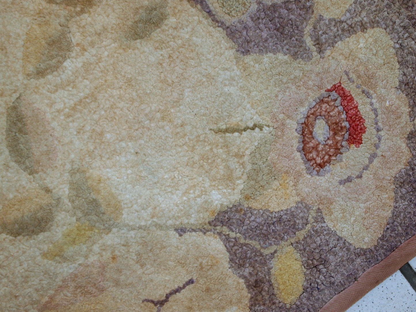 Handmade antique American Primitive Hooked rug in beige shade with abstract/floral design. The border is purple. It is in good condition.