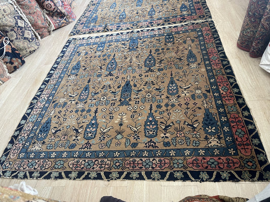 Close-up of a hand-knotted 1880s Indian Agra rug showing tall steel blue cypress trees, blooming flowers in ivory, blush pink, teal, and sage, plus dark songbirds perched on flowering branches.

