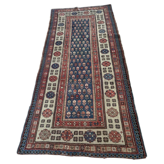 Full view of an antique Caucasian Talish wool rug from the 1880s, featuring a deep indigo navy field with a dense allover lattice of stylized floral rosettes and leaf forms, framed by an exceptionally wide ivory main border with large octagonal rosette medallions in terracotta red and midnight navy.

