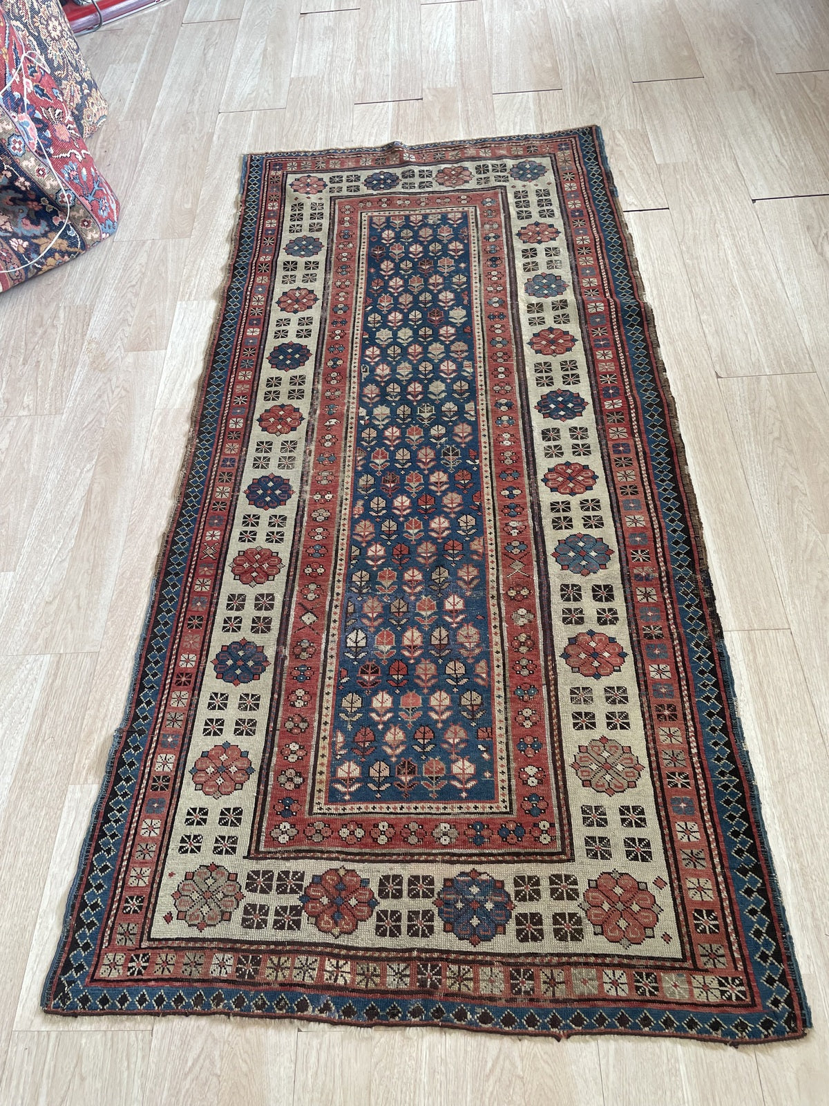 Close-up of the wide ivory main border on a 1880s Talish rug, showing a stately procession of large octagonal rosette medallions with concentric rings, hooked arms, and central star forms in deep terracotta red and navy.

