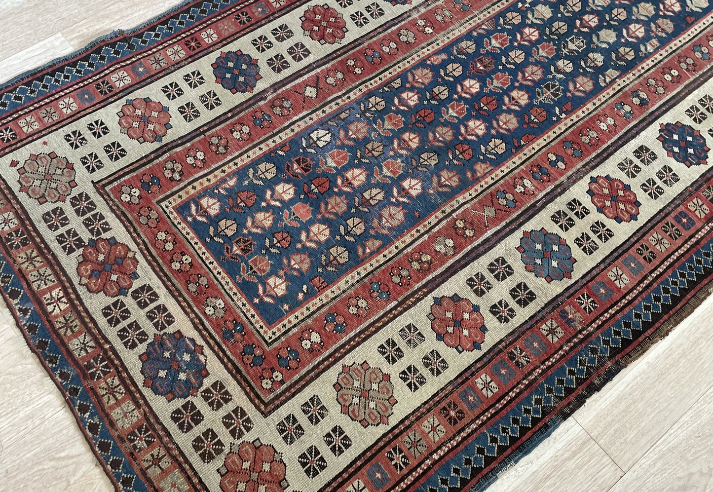 Detail of the allover field lattice on an antique Talish rug, showing tightly packed stylized floral rosettes and leaf forms in ivory, terracotta red, sage green, and warm camel arranged in diagonal rows.


