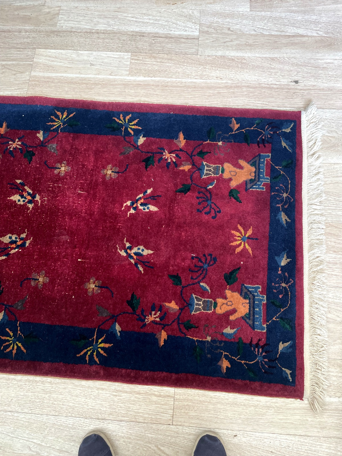 Close-up of an antique Chinese Art Deco carpet showing a butterfly pair in ivory and coral against the crimson field, with trailing navy vine tendrils symbolizing joy, longevity, and the freedom of the soul in Chinese culture.

