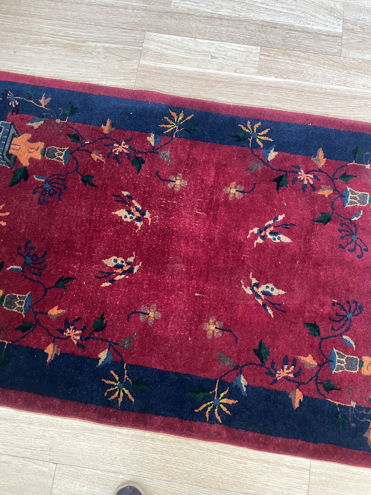 Details of the wide midnight navy border on a 1920s Art Deco Chinese rug, showing scholar's bronze ritual vessels (bāgǔ) in steel blue-grey with saffron orange bases, flanked by floral sprays and leaf forms.

