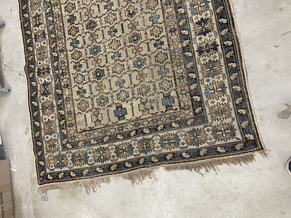 Ivory geometric rug with worn edges and uneven fringe remnants