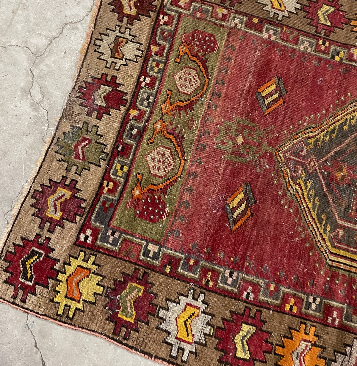 Angled detail of the taupe serrated border, olive floral panel and red field.