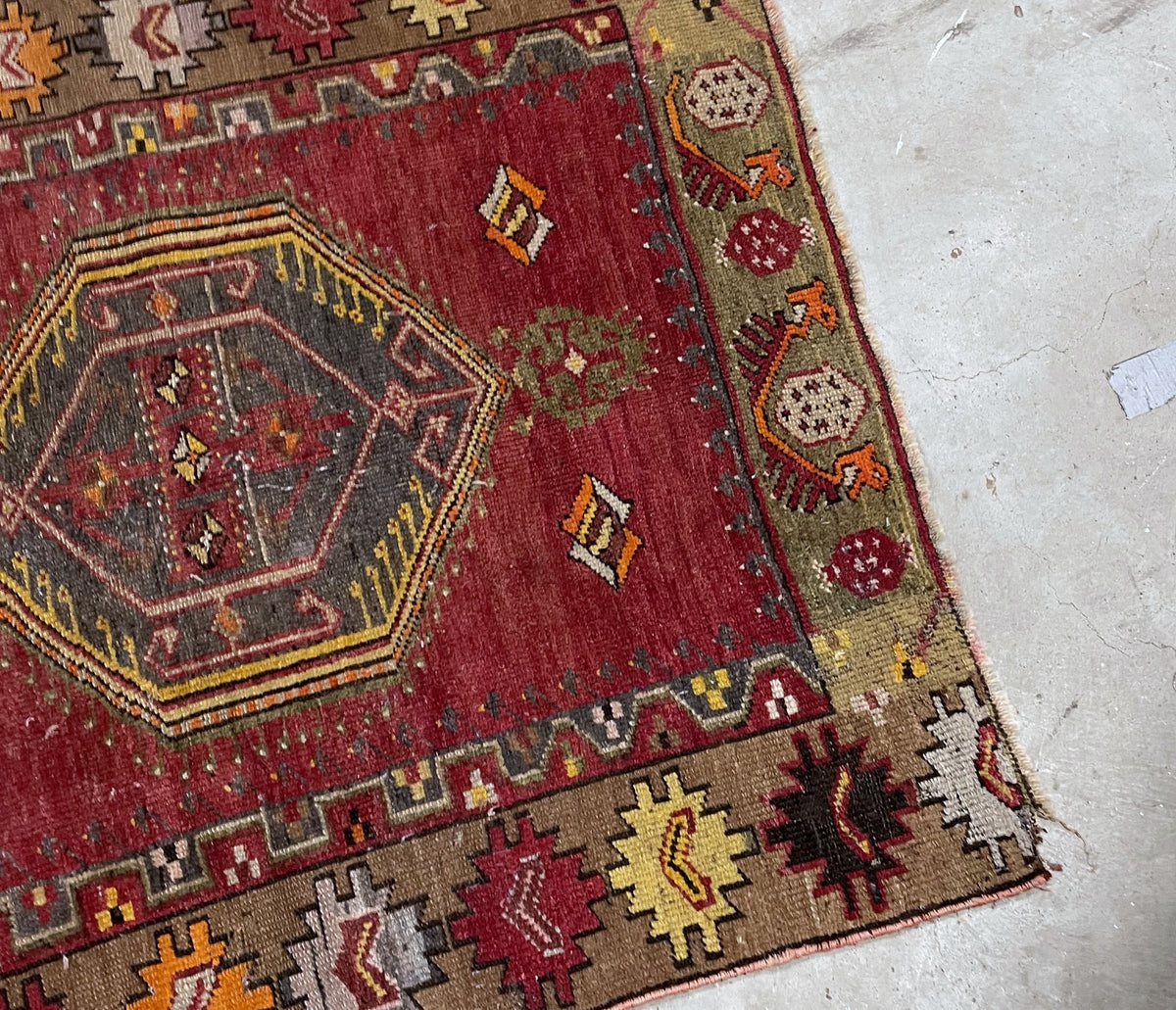 Horizontal view of the red wool rug with geometric medallion and repeating border ornaments.