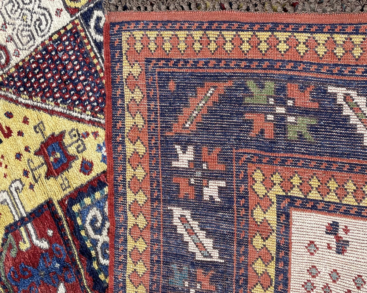 Angled corner view showing ivory field, square ornaments, navy border and brown fringe remnants.