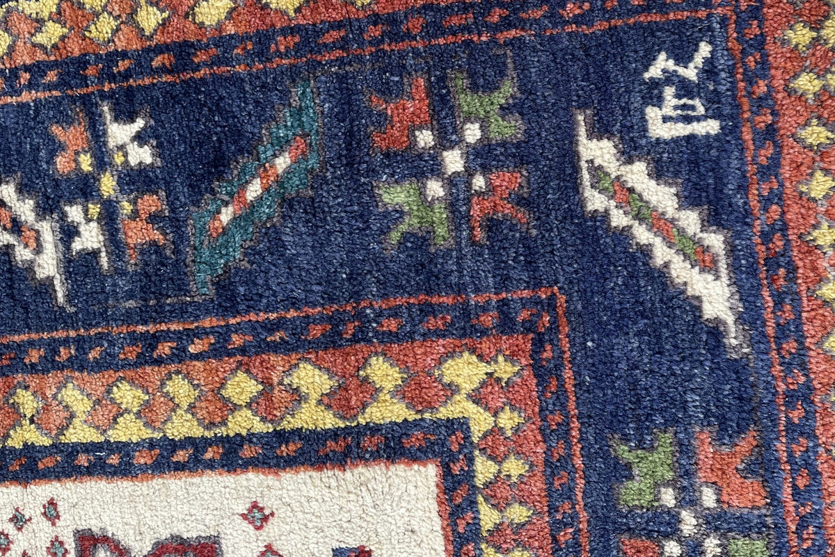 Rug corner showing navy border, yellow-and-red guard bands and uneven brown fringe.