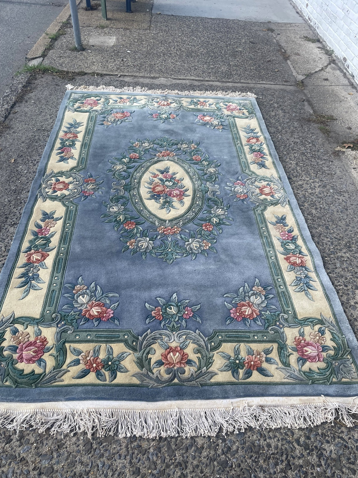 Folded rug corner revealing the woven reverse, blue binding and uneven white fringe.
