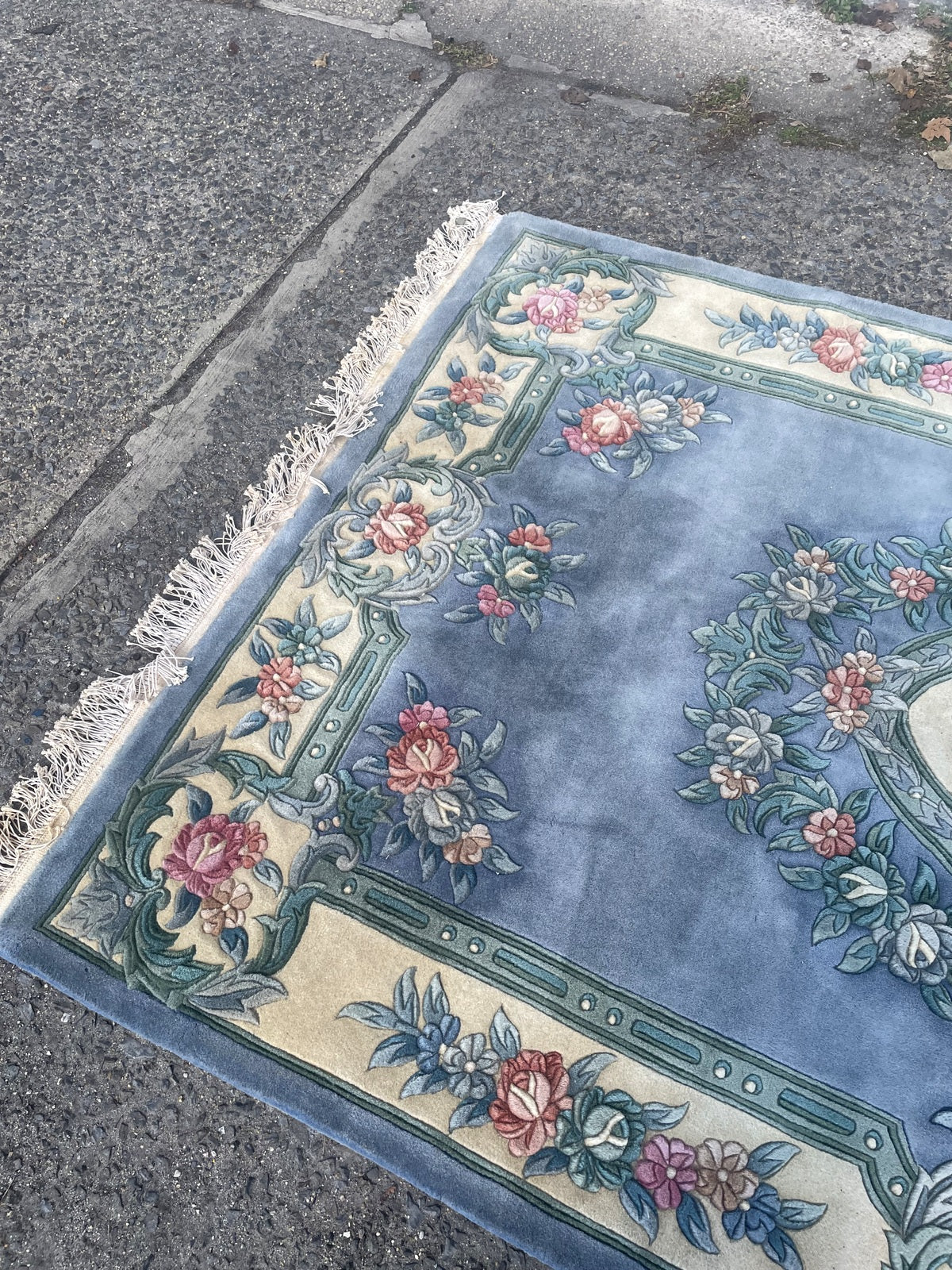 Full view of the blue wool rug with central floral wreath and broad ivory border.