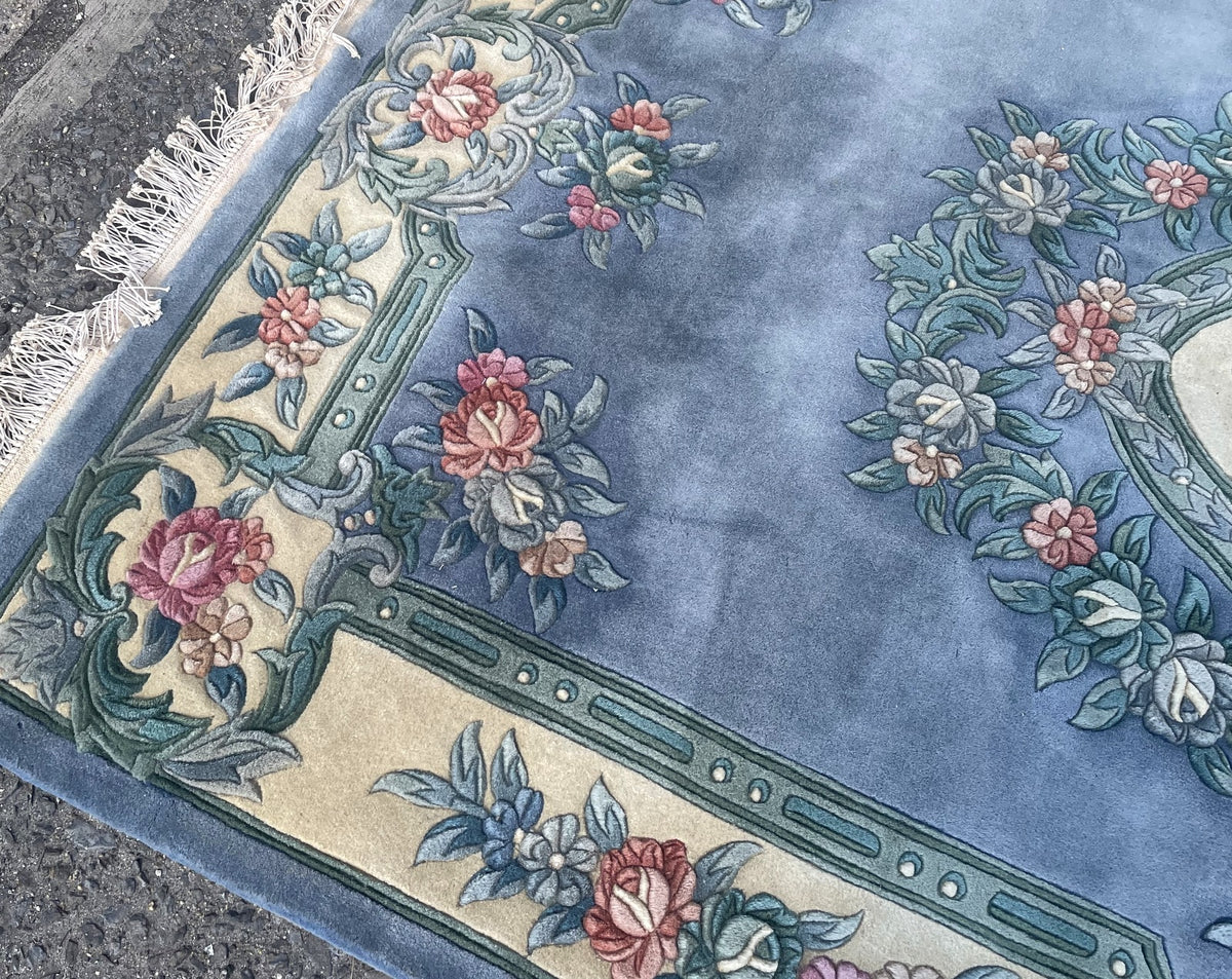 Sculpted pink roses and sage-green scrollwork at an ivory border corner beside white fringe.