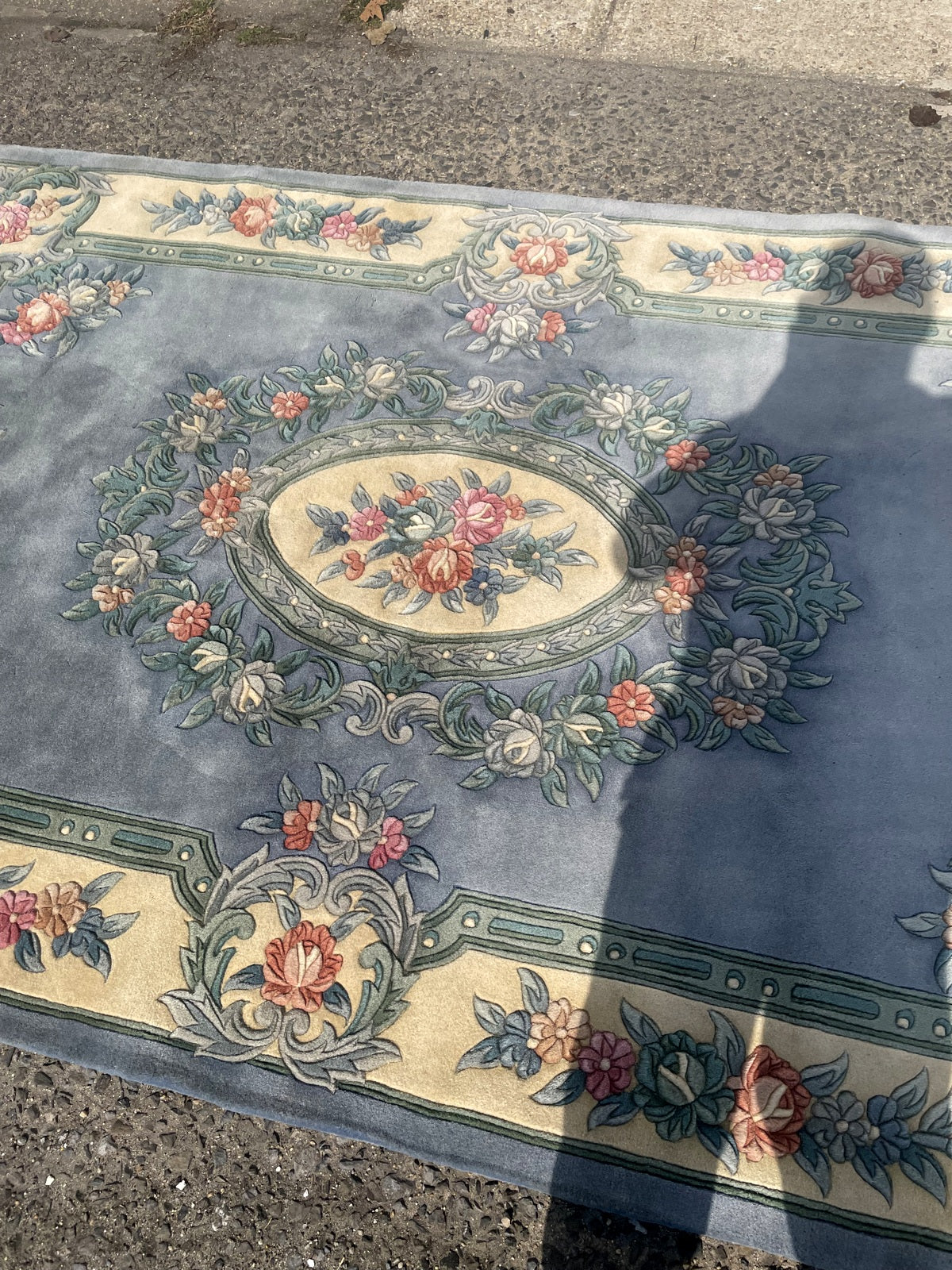 Angled rug end showing floral cartouches, blue outer edging and uneven fringe.