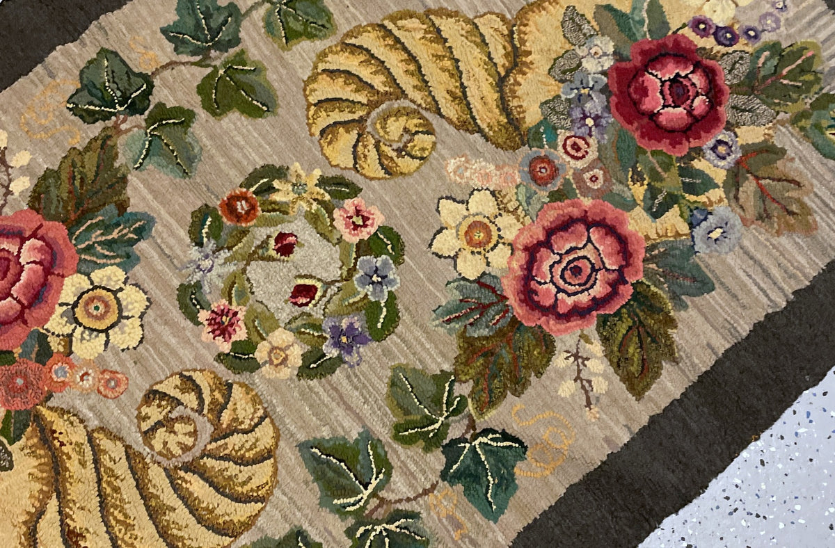 Angled detail of a golden horn, shaded rose blooms, ivy and the central floral wreath.