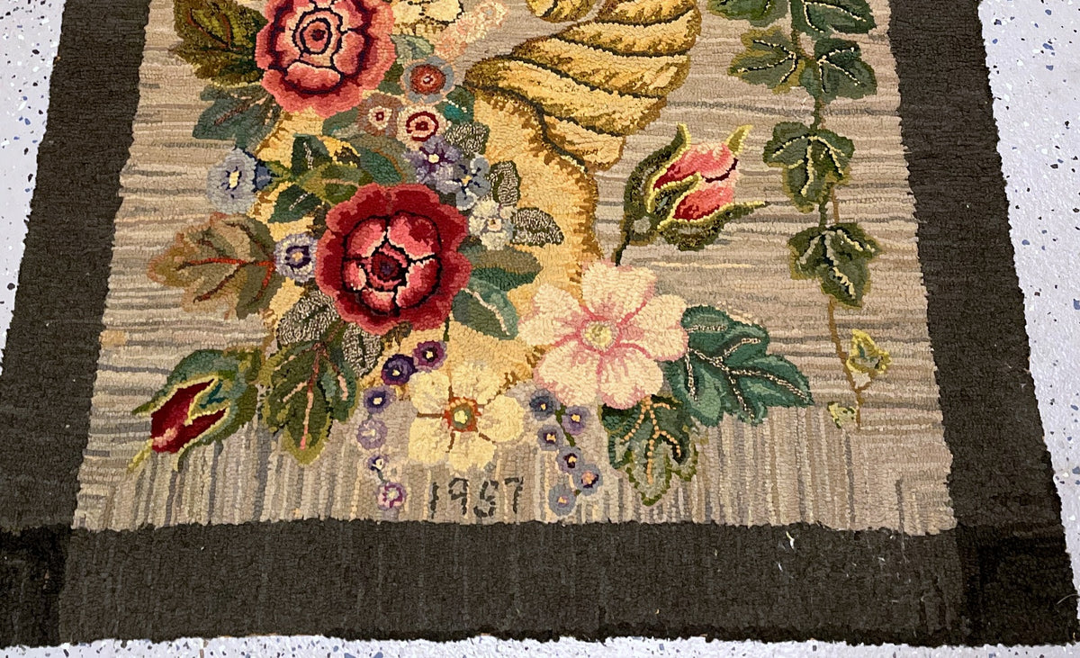 Horizontal view of the hooked rug with striated beige field and dark rectangular border.