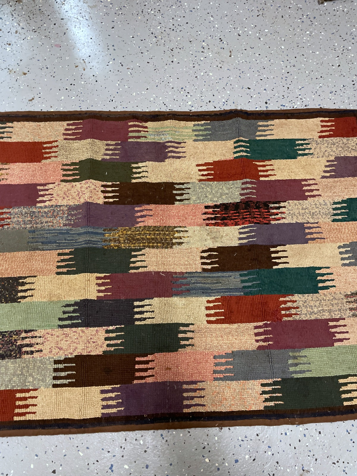 Angled rug corner showing brown binding and pale, dark green and striped blocks.
