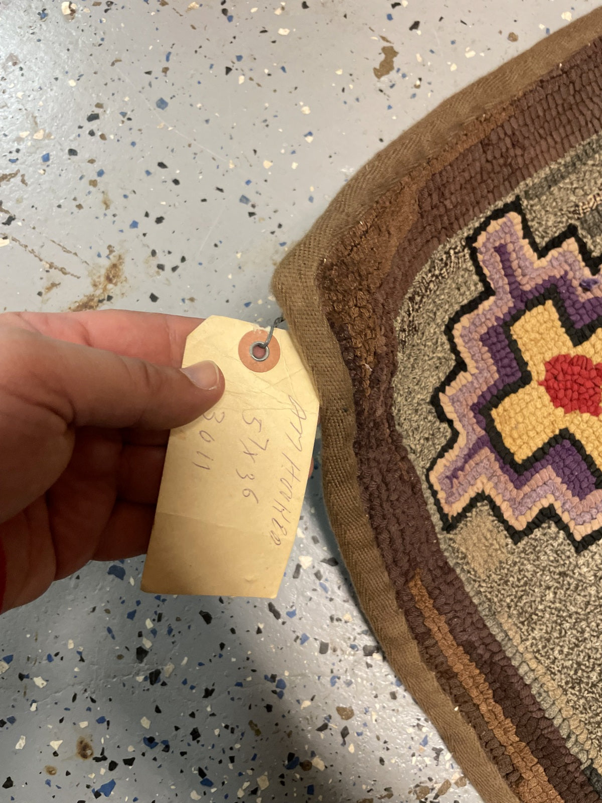 Worn brown rug corner and binding beside an attached handwritten sales tag.