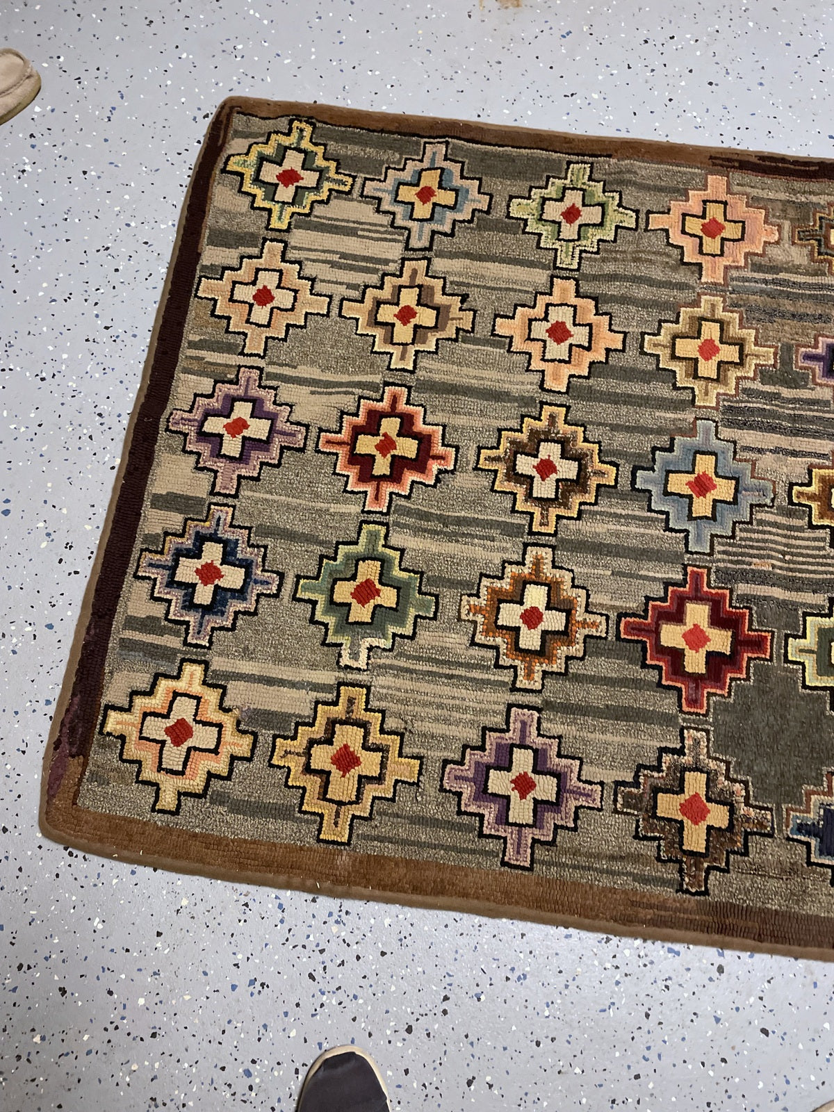 Angled rug view showing rows of multicoloured geometric crosses and brown edging.