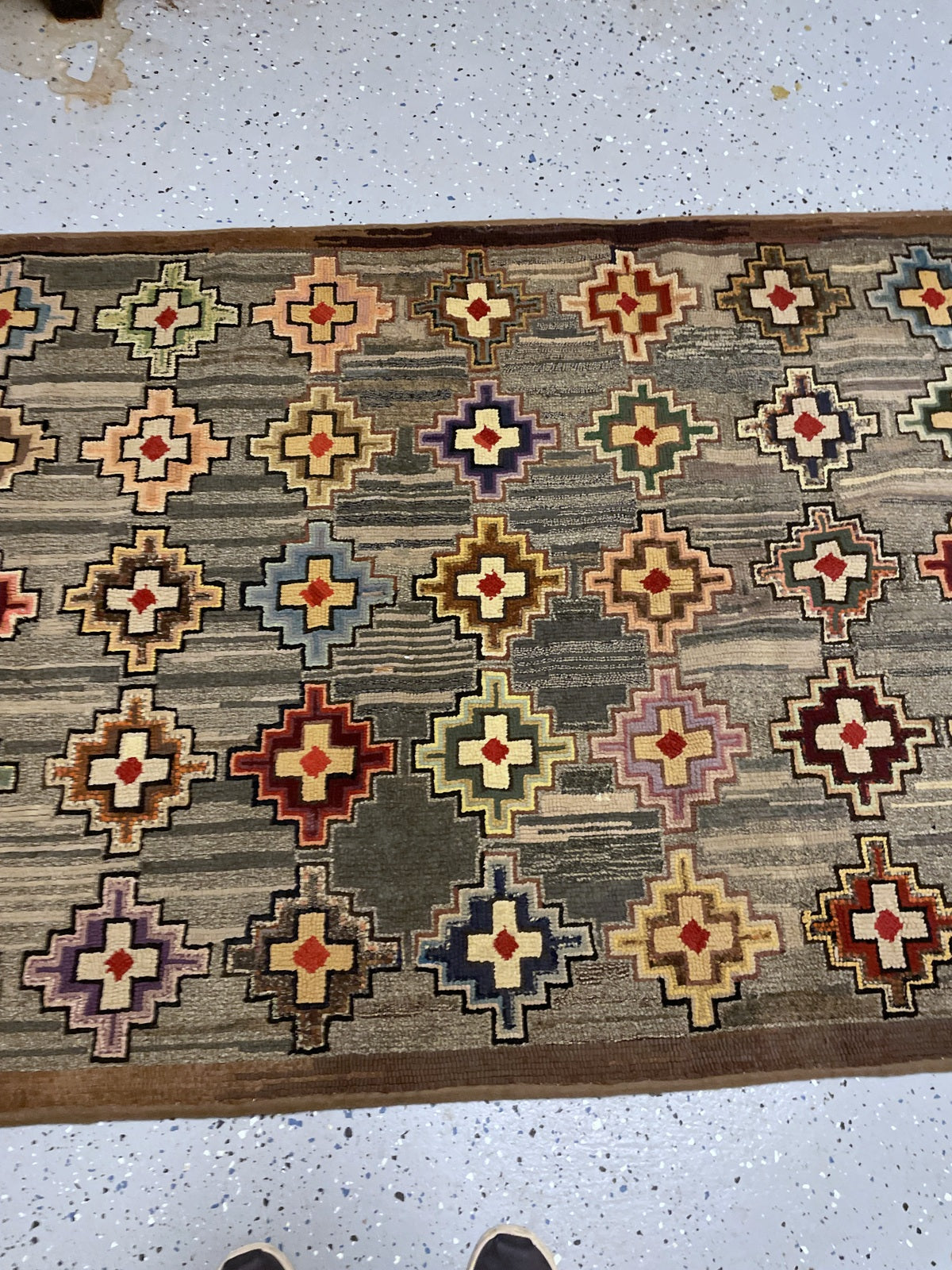 Angled rug end showing pale crosses, coloured stepped outlines and perimeter wear.