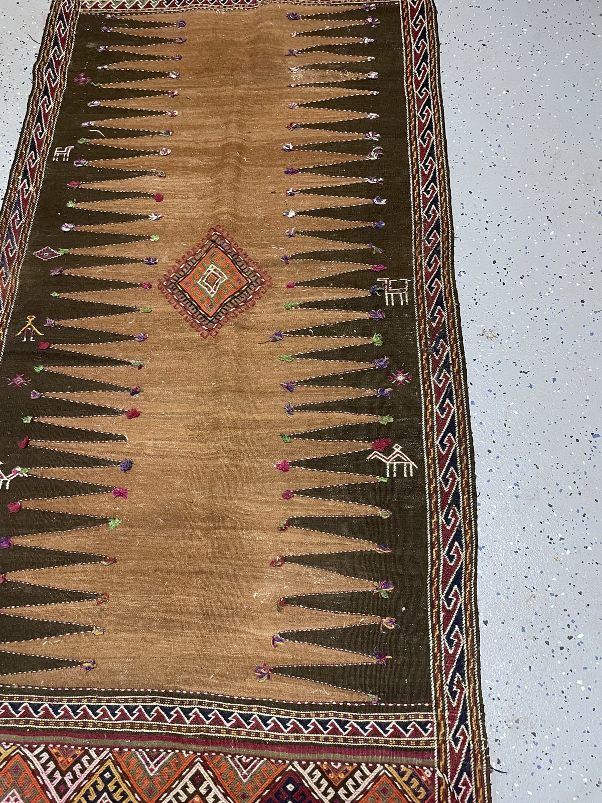 Angled detail of the orange and green diamond medallion with pale stitching and pink and purple tufts.