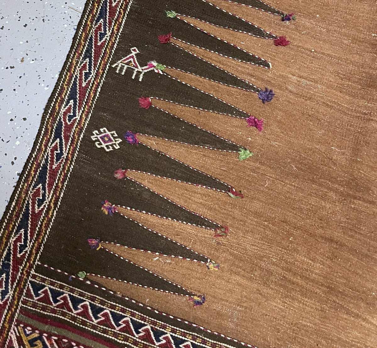 Side detail showing a small human figure, outlined animals and ivory hooked border on burgundy.