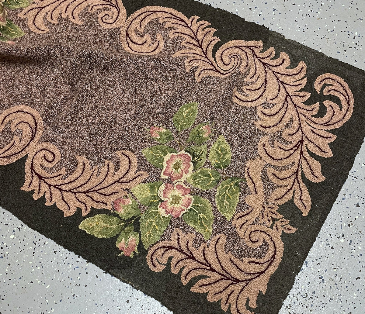 Turned-back rug corner revealing black fabric binding, tan woven foundation and the reverse of the pink scroll design.