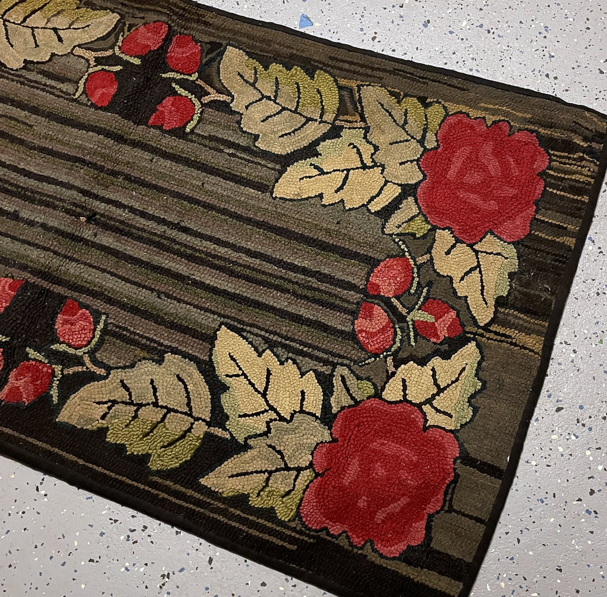 Detailed red roses and shaded cream leaves beside brown stripes and small gaps in the hooked wool surface.