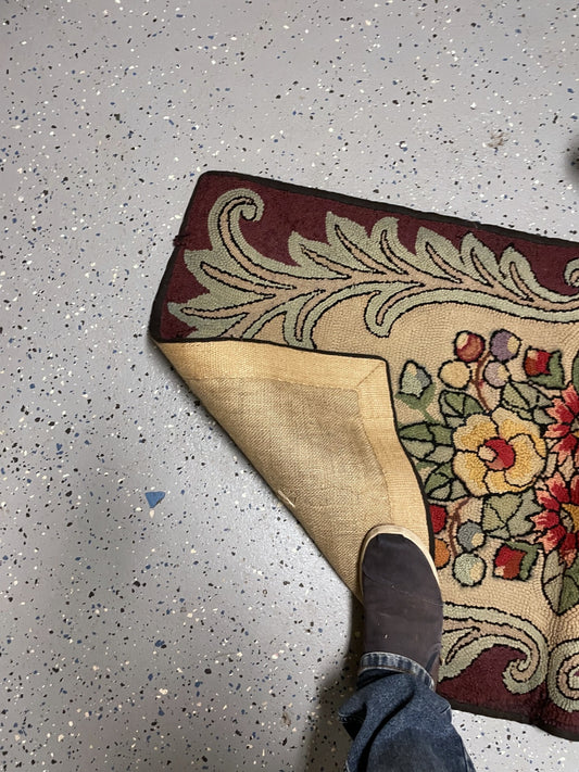 Turned-back rug corner showing tan woven backing beneath the cream floral field and sage scroll border.