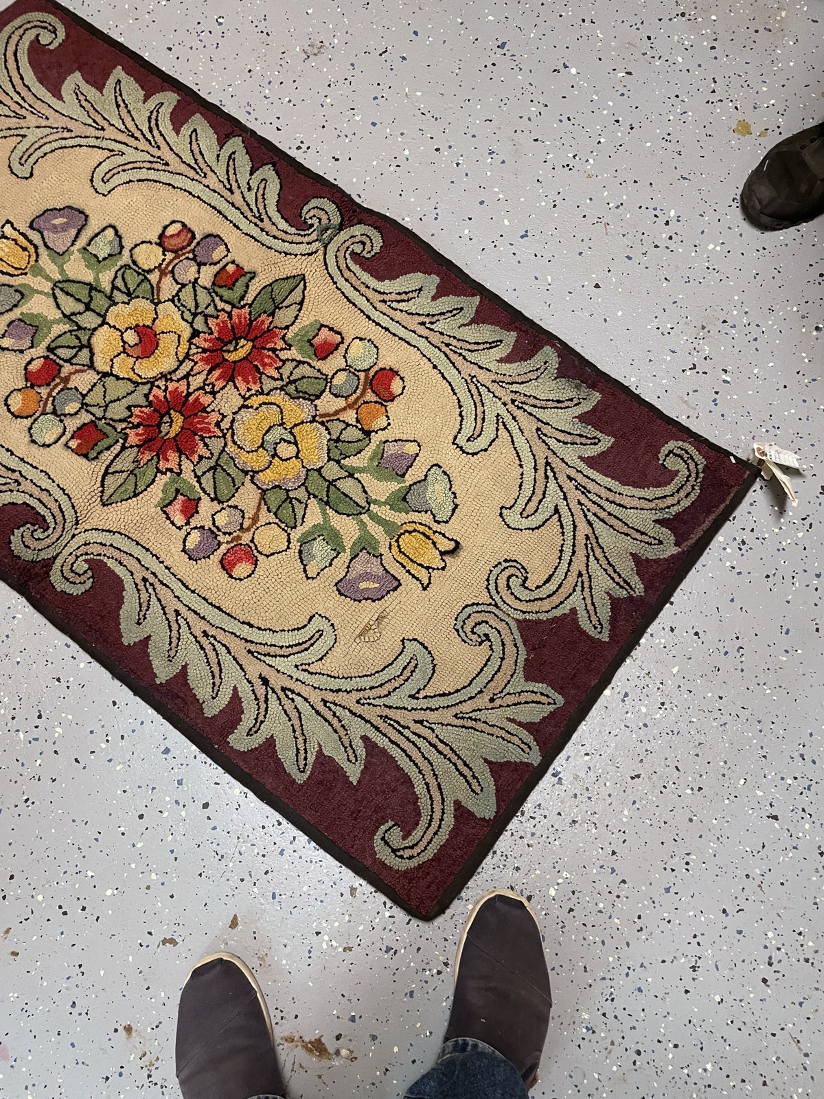 Angled rug end showing curling sage acanthus leaves against burgundy around the cream floral centre.