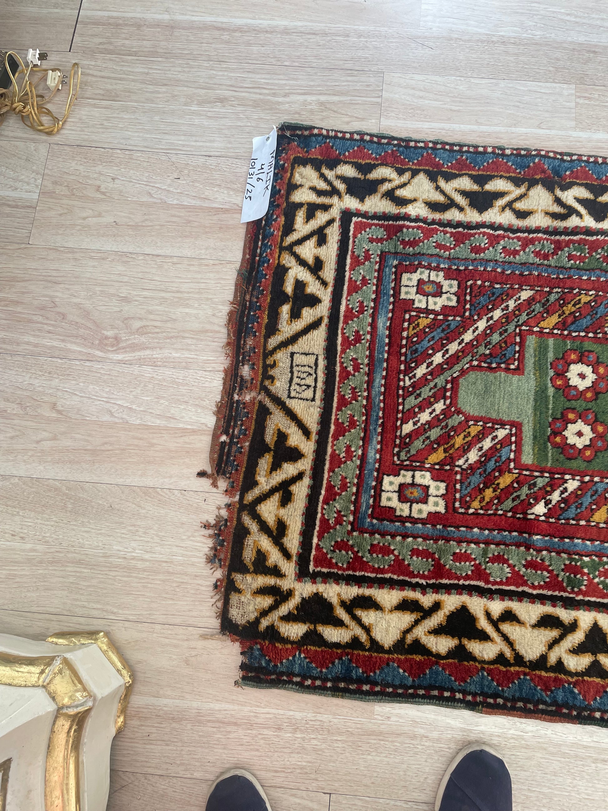 Close-up of a tribal Kazak rug's wool pile, displaying saturated colors of green, red, blue, cream, and black.

