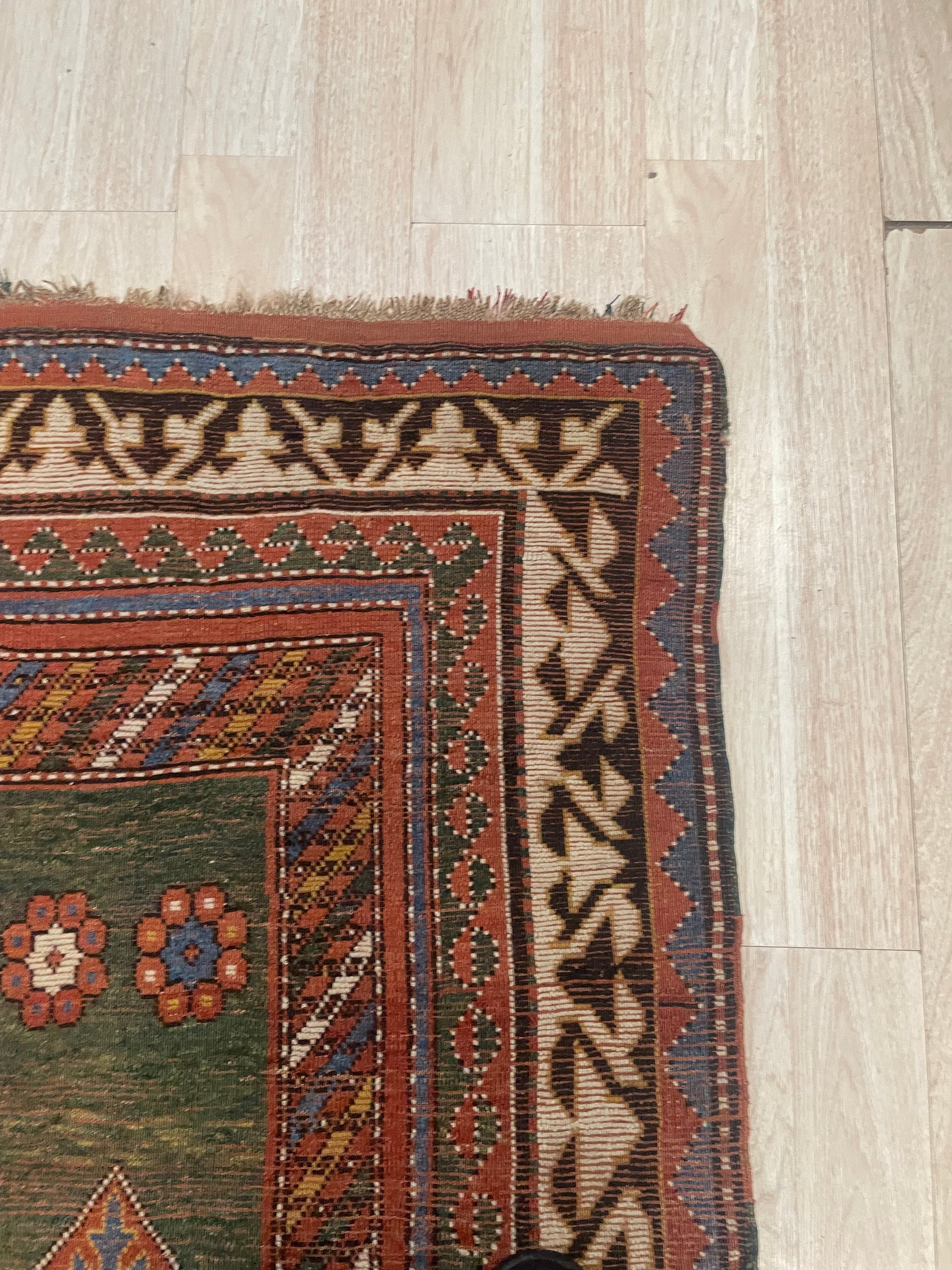 Richly layered borders with geometric guard stripes framing the central green field of an antique Caucasian carpet.

