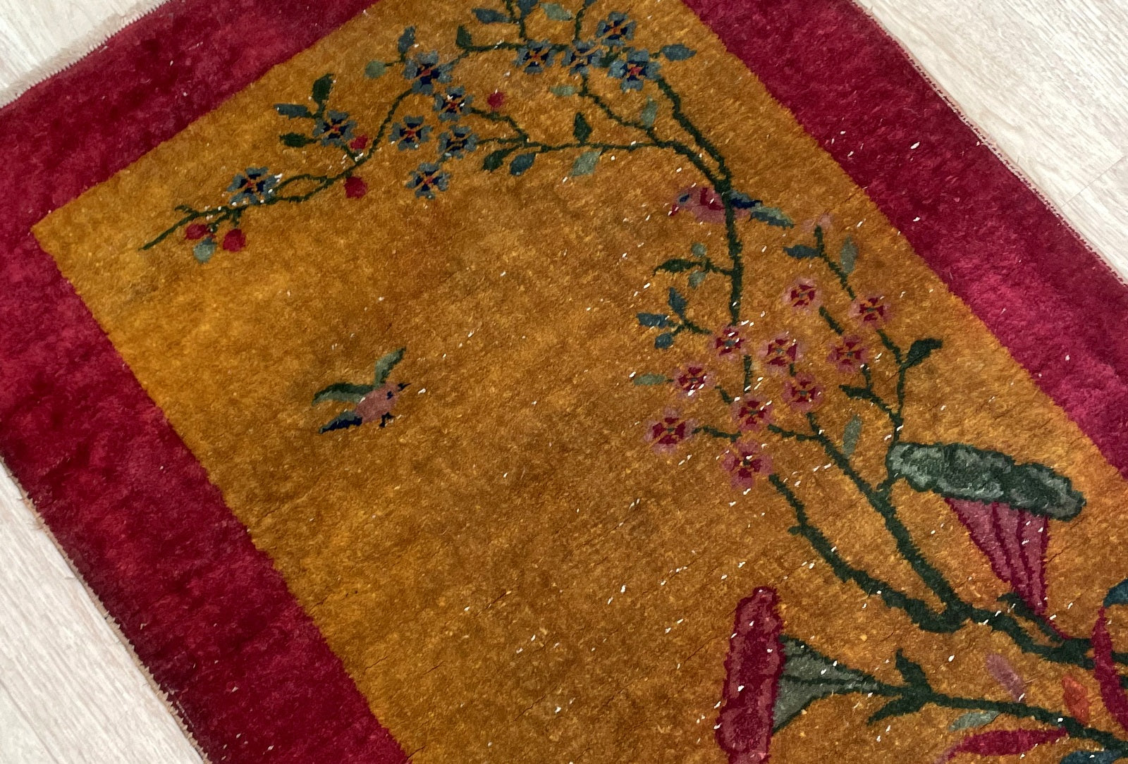 Close-up of antique Chinese Art Deco rug displaying delicate flowering branch and small bird in flight

