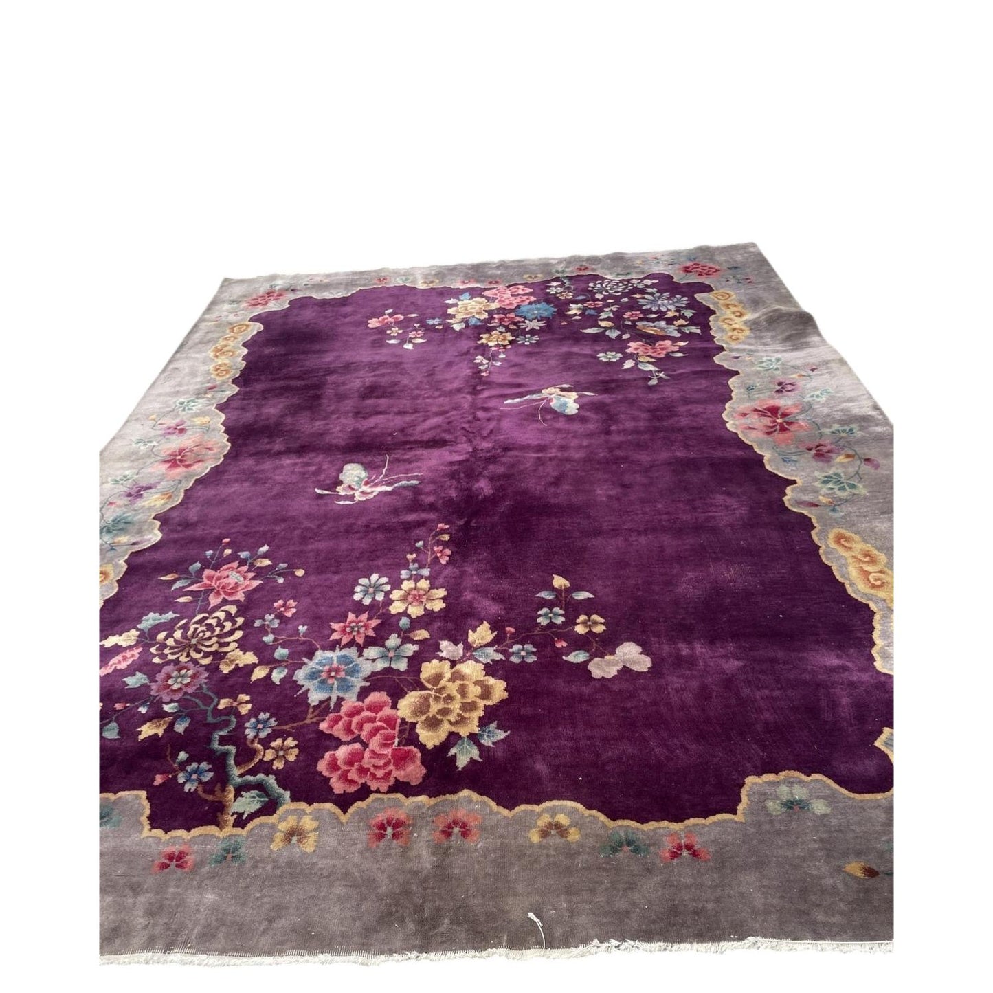 Full view of an antique Art Deco Chinese wool rug from the 1920s featuring a deep aubergine plum field with an asymmetric cascade of oversized floral blooms including peonies, chrysanthemums, and cherry blossoms.

