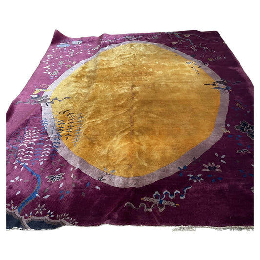 Full view of an antique Art Deco Chinese wool rug from the 1920s featuring a large golden amber oval medallion ringed in blush pink against a deep burgundy plum field.

