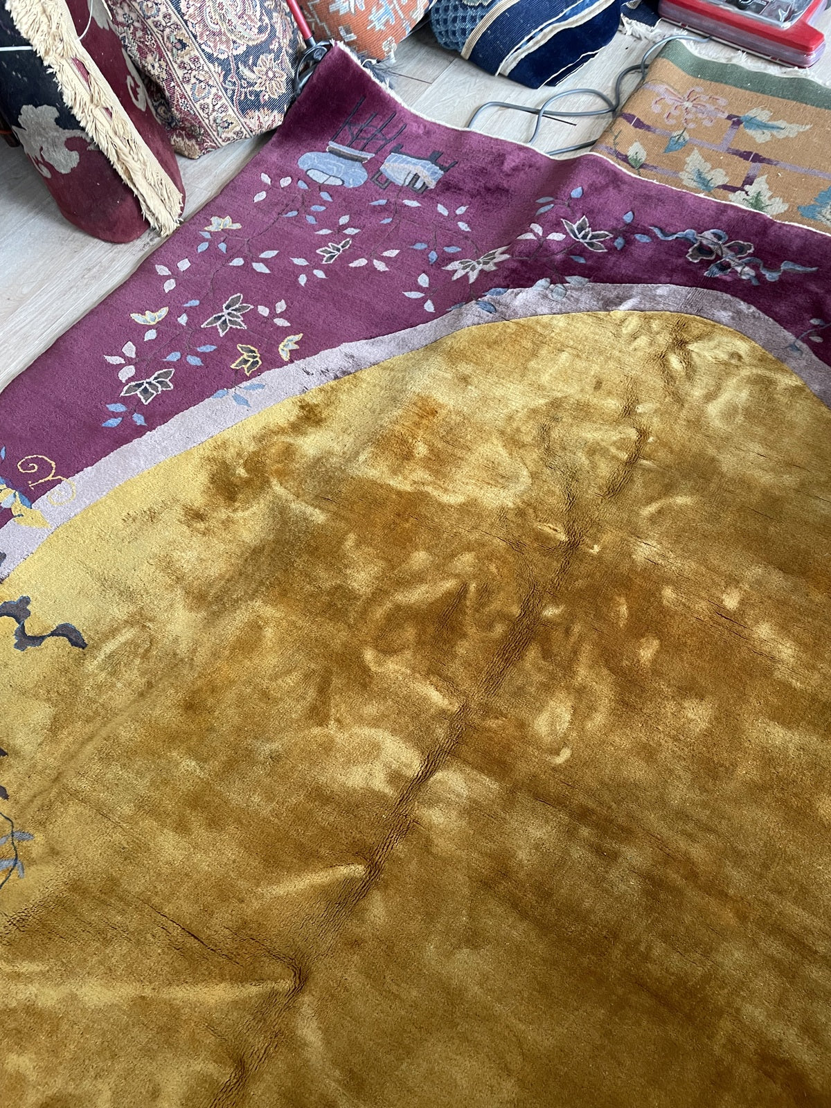 Collector-quality 1920s Chinese rug with a golden amber medallion, dark charcoal peonies in the corners, and ruyi cloud scrolls in teal and ivory on a plum ground.

